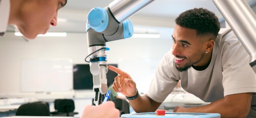 Two young engineers studying a robotic arm 