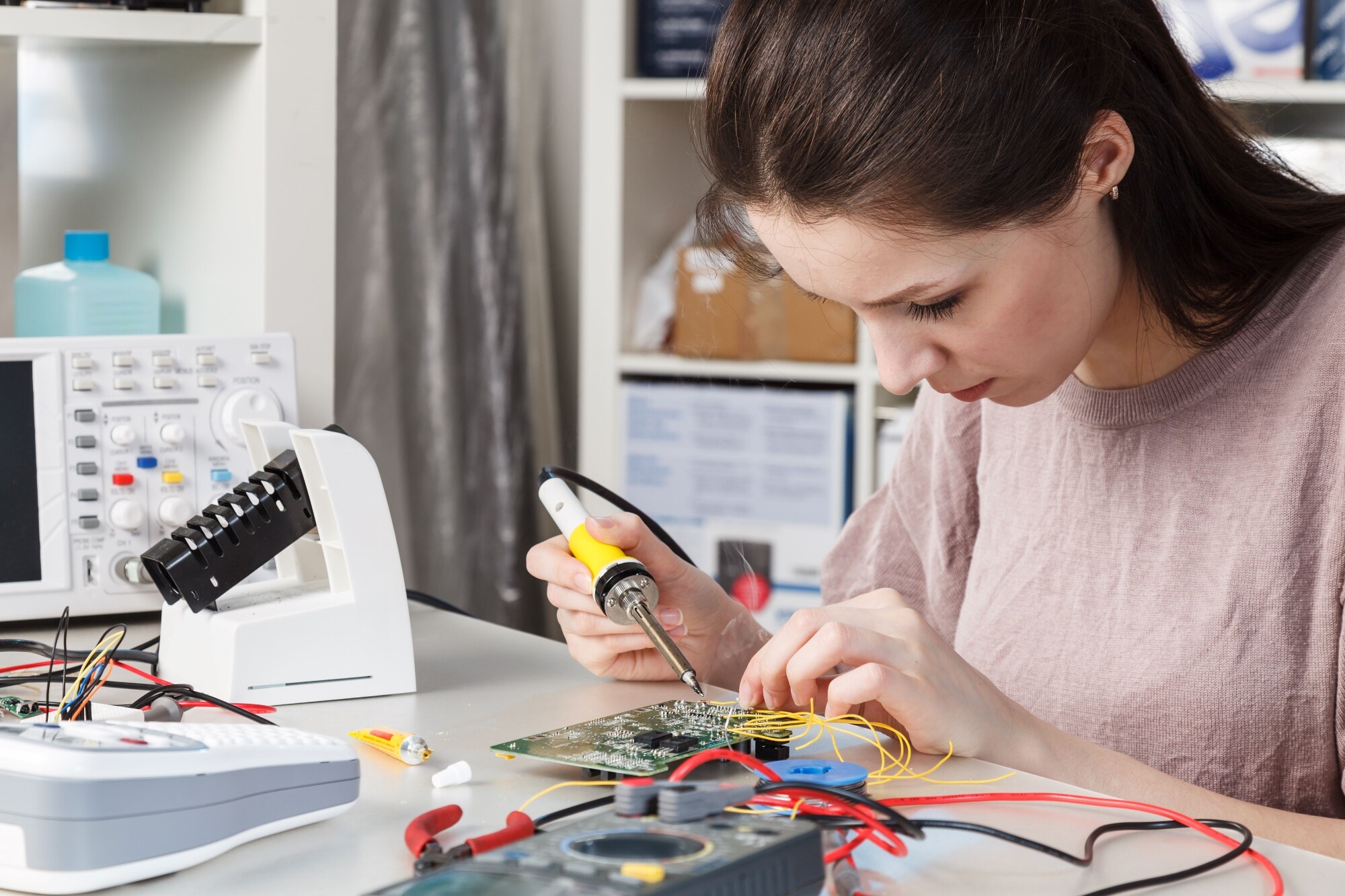 A woman soldering electronic components on a circuit board.