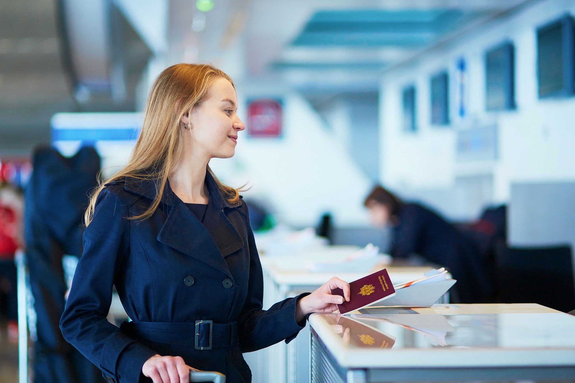 Person holding a passport and boarding pass, standing at an airport check-in counter.