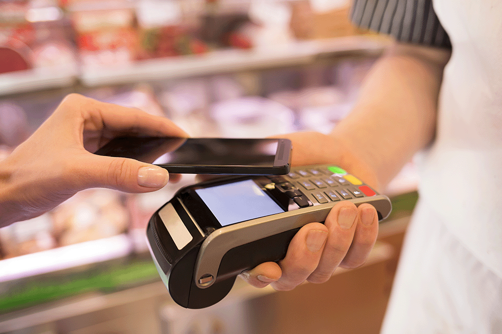 Person making a contactless payment with a smartphone on a card reader held by a cashier. 