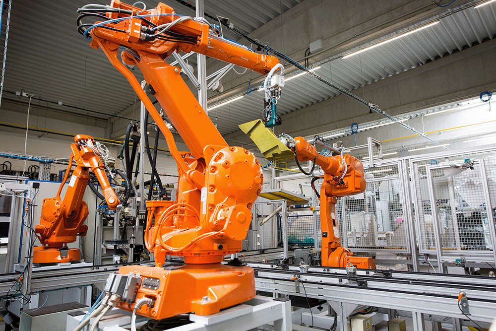 Orange industrial robotic arms operating on an automated assembly line inside a factory.