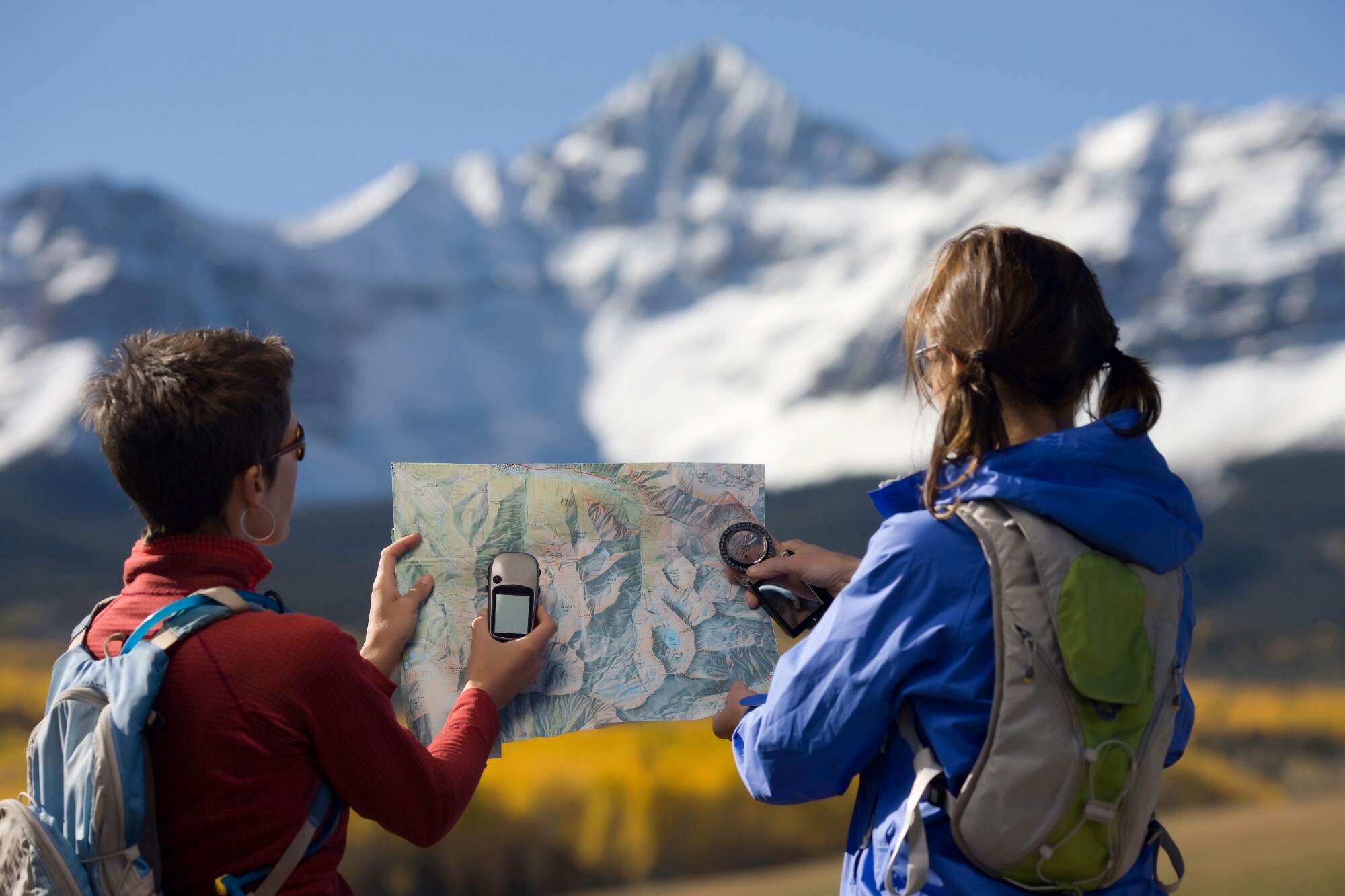 Two hikers with backpacks using GPS devices while navigating in a snowy mountain landscape.