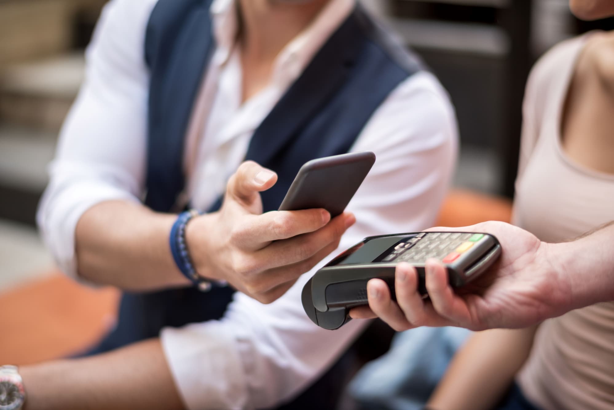 スマートフォンを決済端末に近づけ、非接触決済を行う人と、端末を持っている別の人。