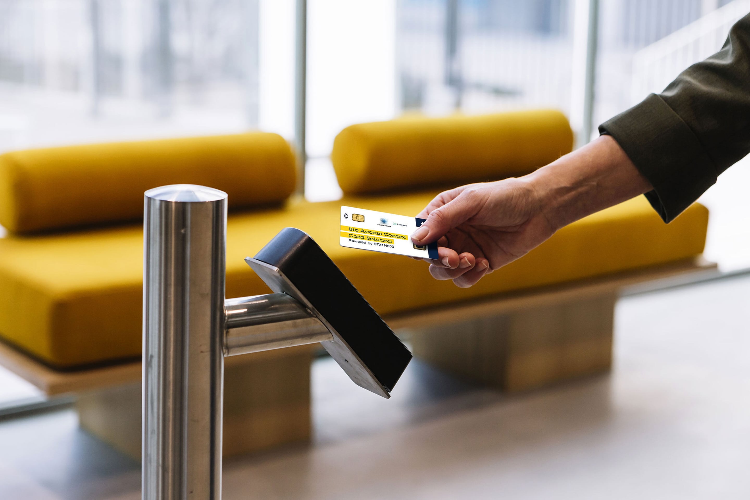 Hand holding bio access control card near a card reader in a modern lobby.