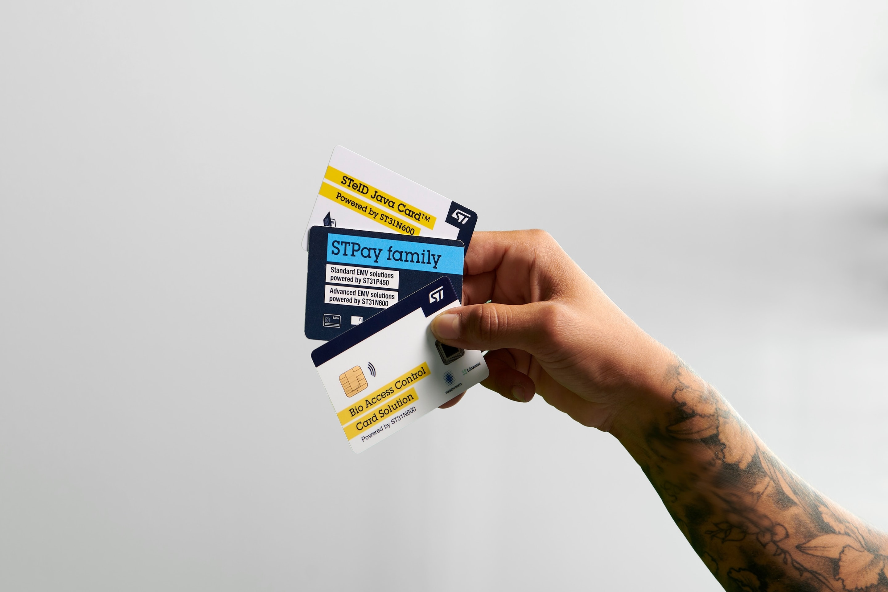 Hand holding three cards: a 'Bio Access Control Card Solution', an 'STPay family' card, and a 'STID Tap&Go' card, all branded with the STMicroelectronics logo. 