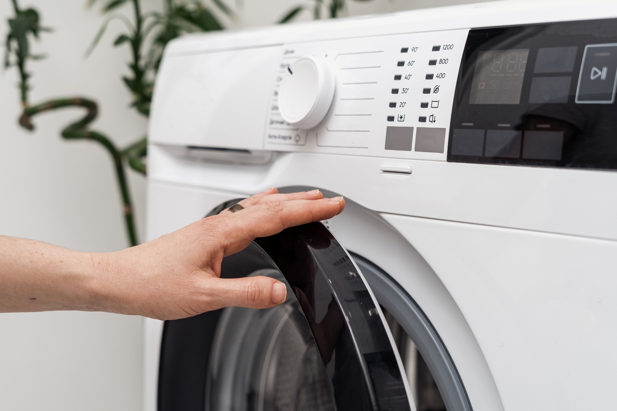 Hand pressing the start button on a washing machine control panel. 